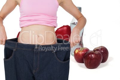 Midsection of woman wearing loose jeans with fruits by drink and boxing gloves in background
