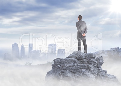 Business man standing on rock looking at misty skyline