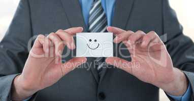 Midsection of businessman holding smiley face on card