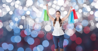Happy woman with arms raised holding shopping bags over bokeh