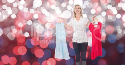Happy woman holding dresses over bokeh
