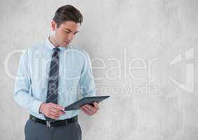 Young businessman holding digital tablet against wall