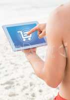 Person in swim wear on beach using Tablet with Shopping trolley icon