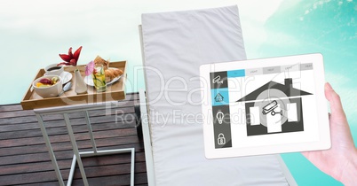 Hand with house application on digital tablet with lounge chair and breakfast in background