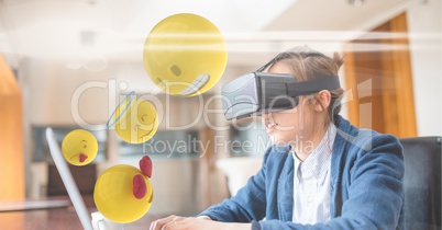 Digitally generated image of emojis flying by businessman wearing VR glasses while using laptop at d