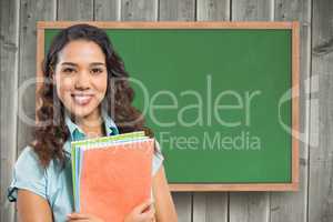 Female student holding book against chalkboard