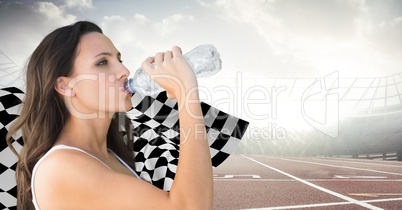 Female runner drinking on track against flares and checkered flag