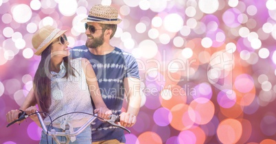 Happy couple riding bicycle during summer vacation over bokeh