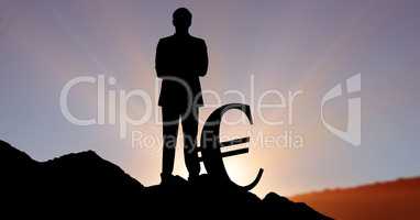 Silhouette businessman standing by euro sign on hill against sky