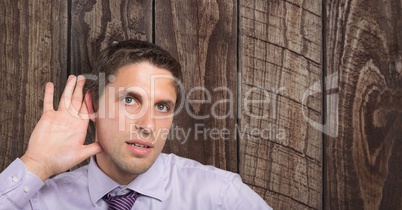 Businessman with hand on ear listening over wooden wall