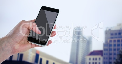 Hand with phone against blurry buildings