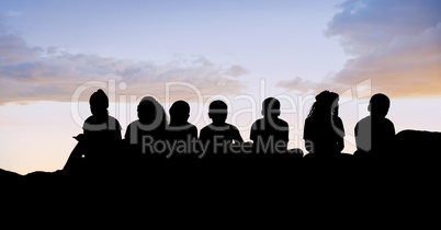 Silhouette kids sitting on hill against sky