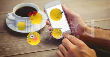 Emojis coming out from smart phone held by man with coffee cup on table