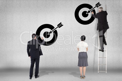 Rear view of business people drawing arrow with target symbol on wall