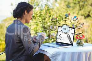 Businesswoman having coffee while looking at laptop with diagrams