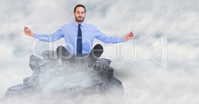 Business man meditating on mountain peak in the clouds