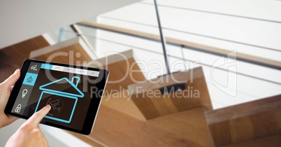 Hands using smart home app on tablet PC with staircase in background