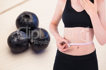 Midsection of woman measuring waist against fruits in background