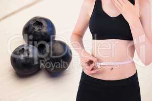 Midsection of woman measuring waist against fruits in background