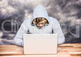 Criminal in hood on laptop in front of clouds