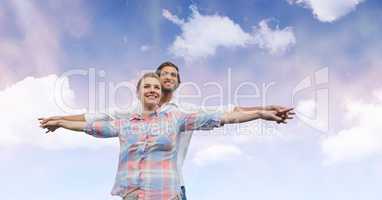 Happy couple with arms outstretched against sky