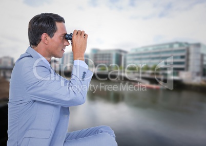 Business man with bionoculars against water across from blurry buildings