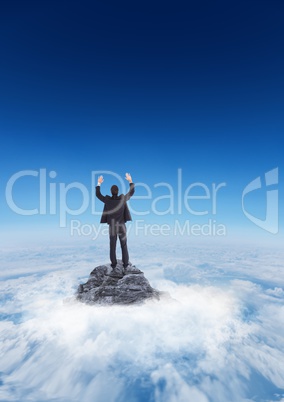 Business man cheering on mountain peak in the clouds