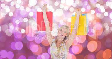 Happy woman with arms raised carrying shopping bags over bokeh