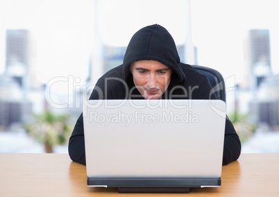 Criminal in hood on laptop by windows