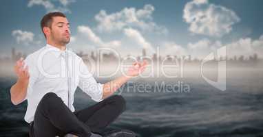 Business man meditating against water and blurry skyline with flare
