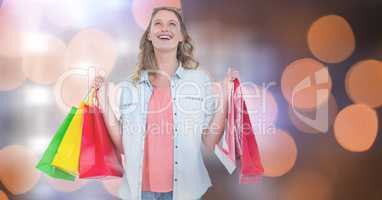 Cheerful woman carrying shopping bags over bokeh