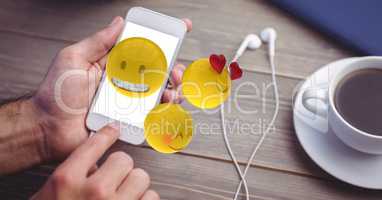 Hands using emojis on smart phone by earphones and coffee cup on table