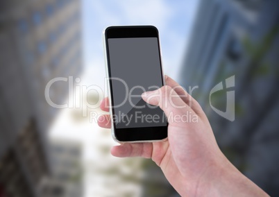 Hand with phone against blurry buildings and sky