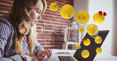 Young woman using laptop while emojis flying over