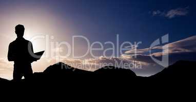 Silhouette businessman using laptop on mountain during sunset