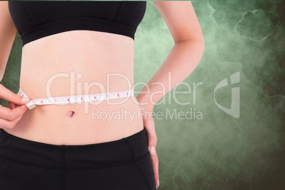 Midsection of woman measuring waist against green background