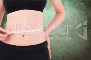 Midsection of woman measuring waist against green background