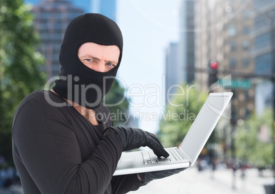 Criminal Man in balaclava on laptop in front of city