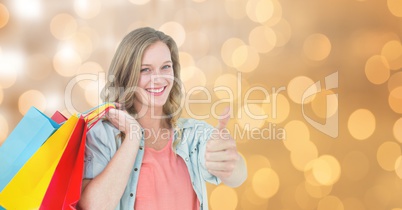 Woman showing thumbs up while holding shopping bags over bokeh