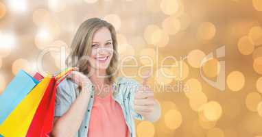 Woman showing thumbs up while holding shopping bags over bokeh
