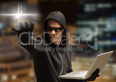 Criminal in hood on laptop in front of night city