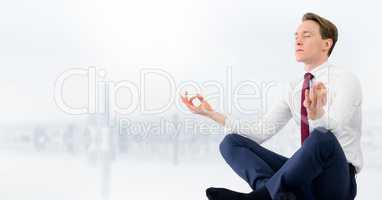 Business man meditating against blurry white skyline