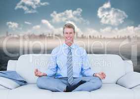 Business man meditating on couch against water and blurry skyline