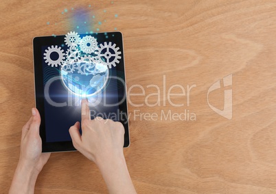 Overhead of hands with tablet showing globe and gear graphics with flares