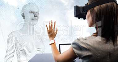 Woman in VR at desk in front of 3D female shaped binary code against sky and clouds