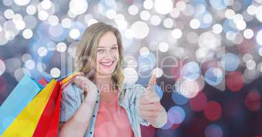 Woman holding shopping bags while gesturing thumbs up over bokeh