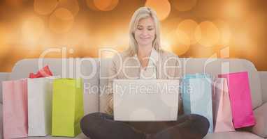 Woman using laptop by shopping bags on sofa over bokeh