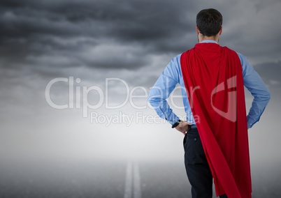 Back of business man superhero with hands on hips against road and stormy sky
