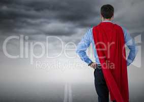 Back of business man superhero with hands on hips against road and stormy sky