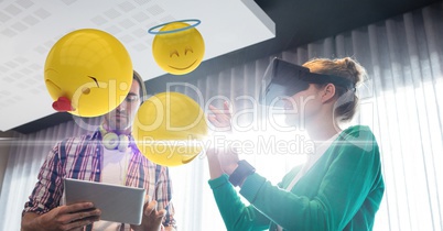 Digital composite image of emojis flying by couple using VR glasses and tablet computer at home